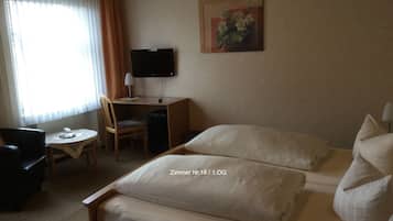 A hotel room with a bed, a desk, a chair, a TV, and a painting on the wall.