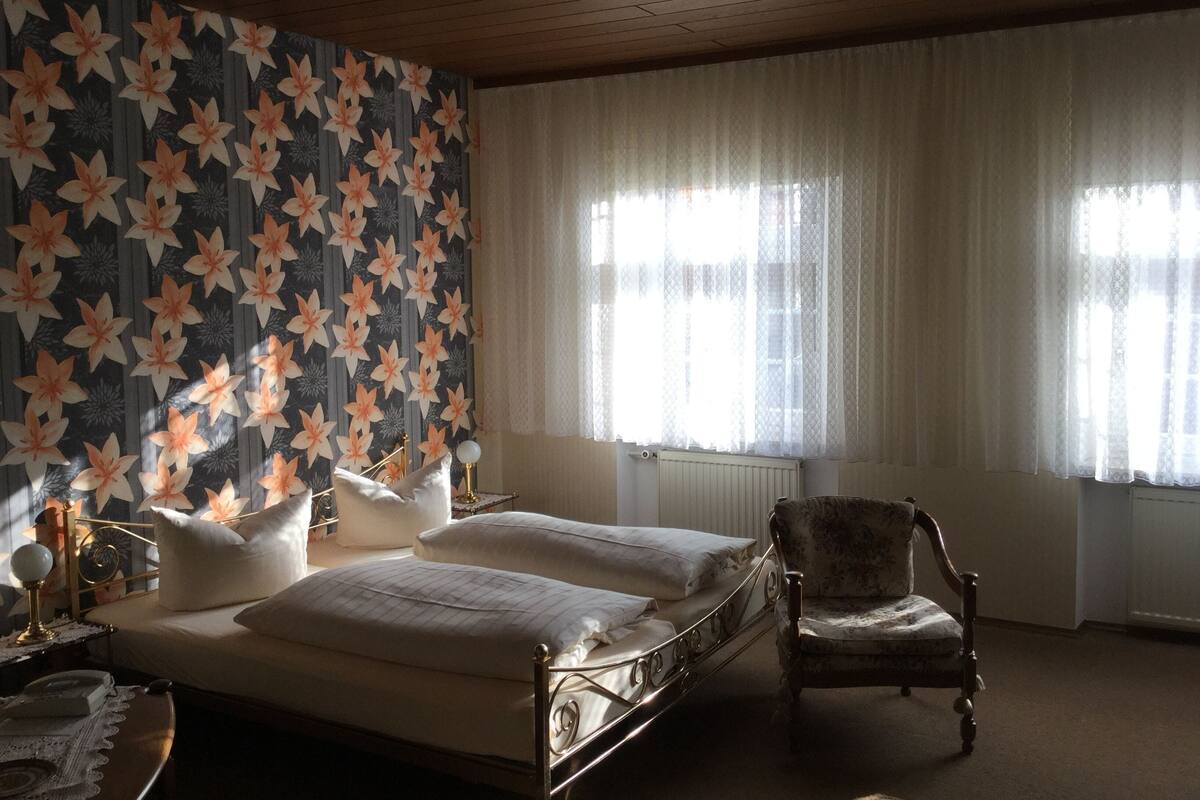 A bedroom with a bed, two bedside tables, a chair, and a window with curtains.