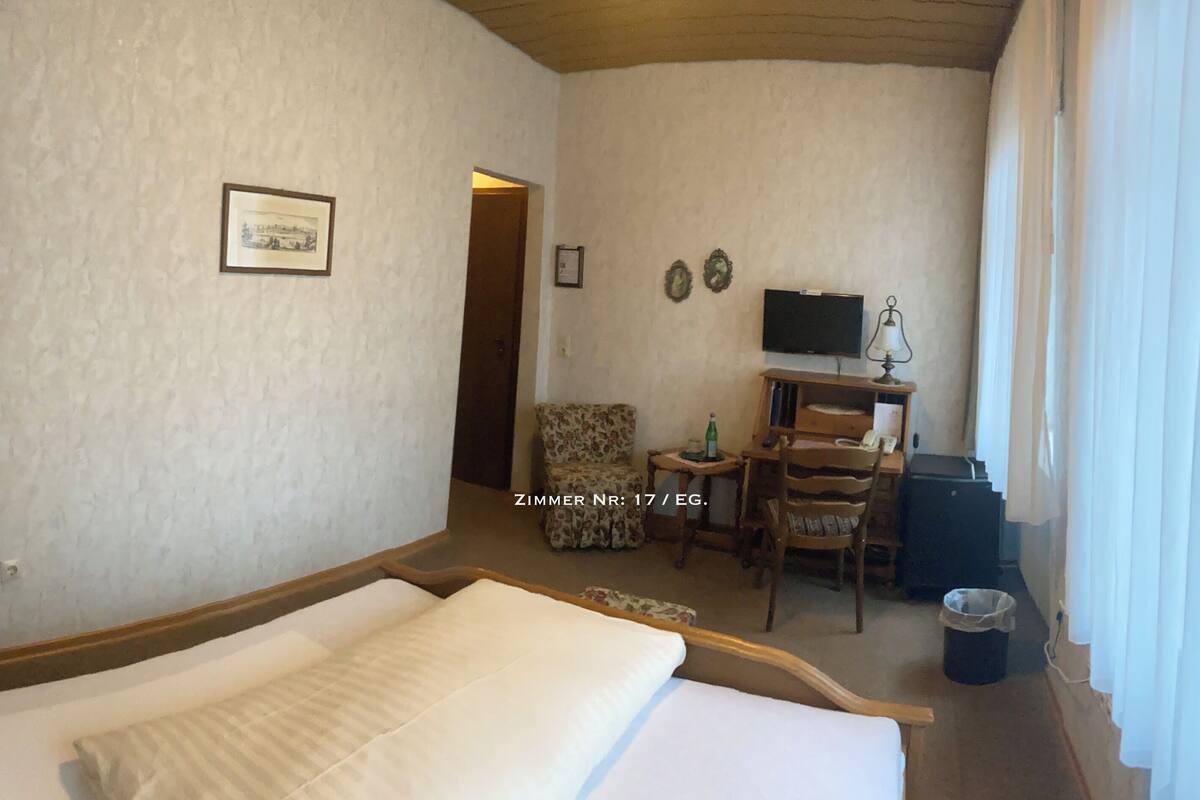 A hotel room with a bed, a desk, a chair, a television, and a window with curtains.
