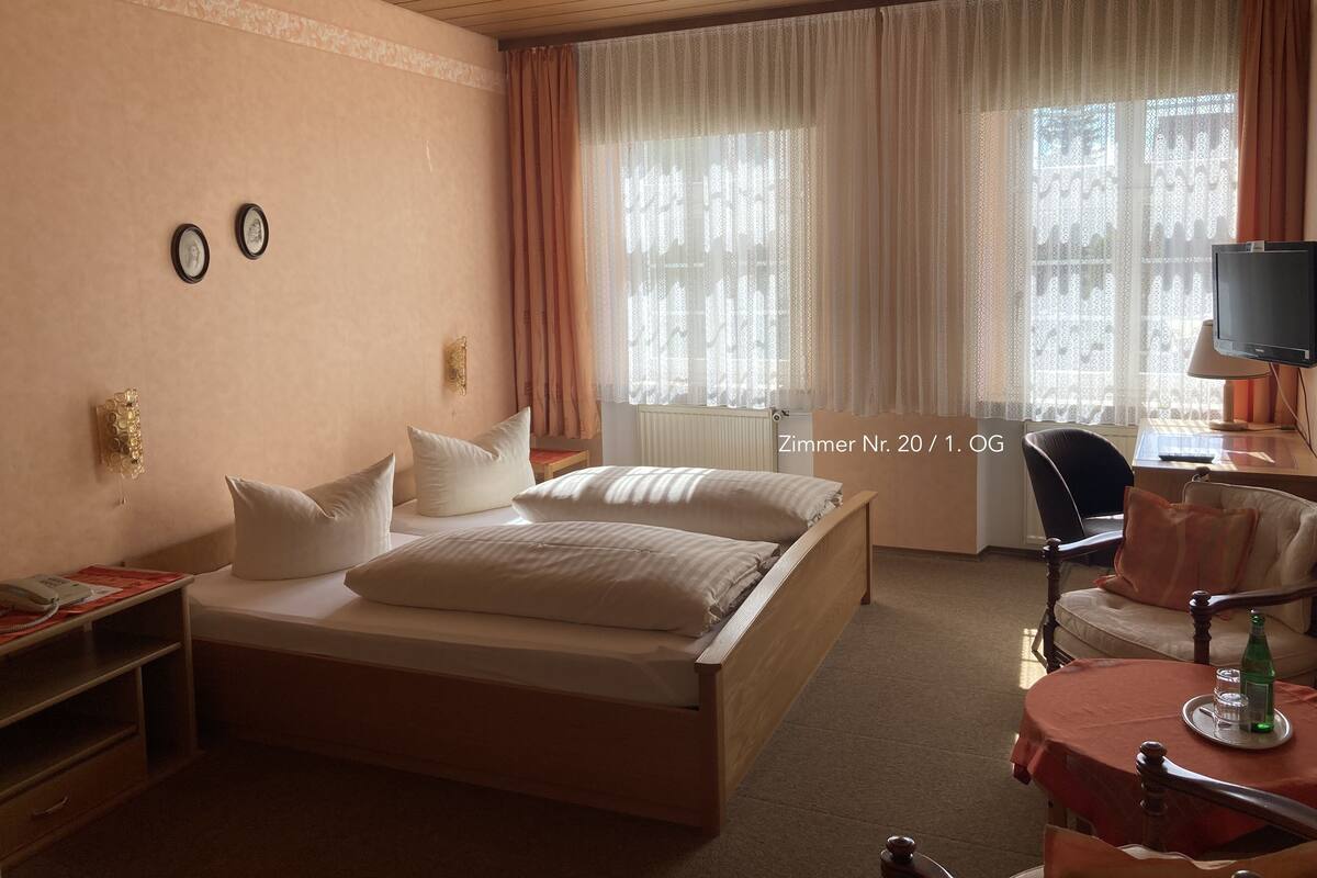 A hotel room with a bed, a desk with a computer, a chair, and a window with curtains.