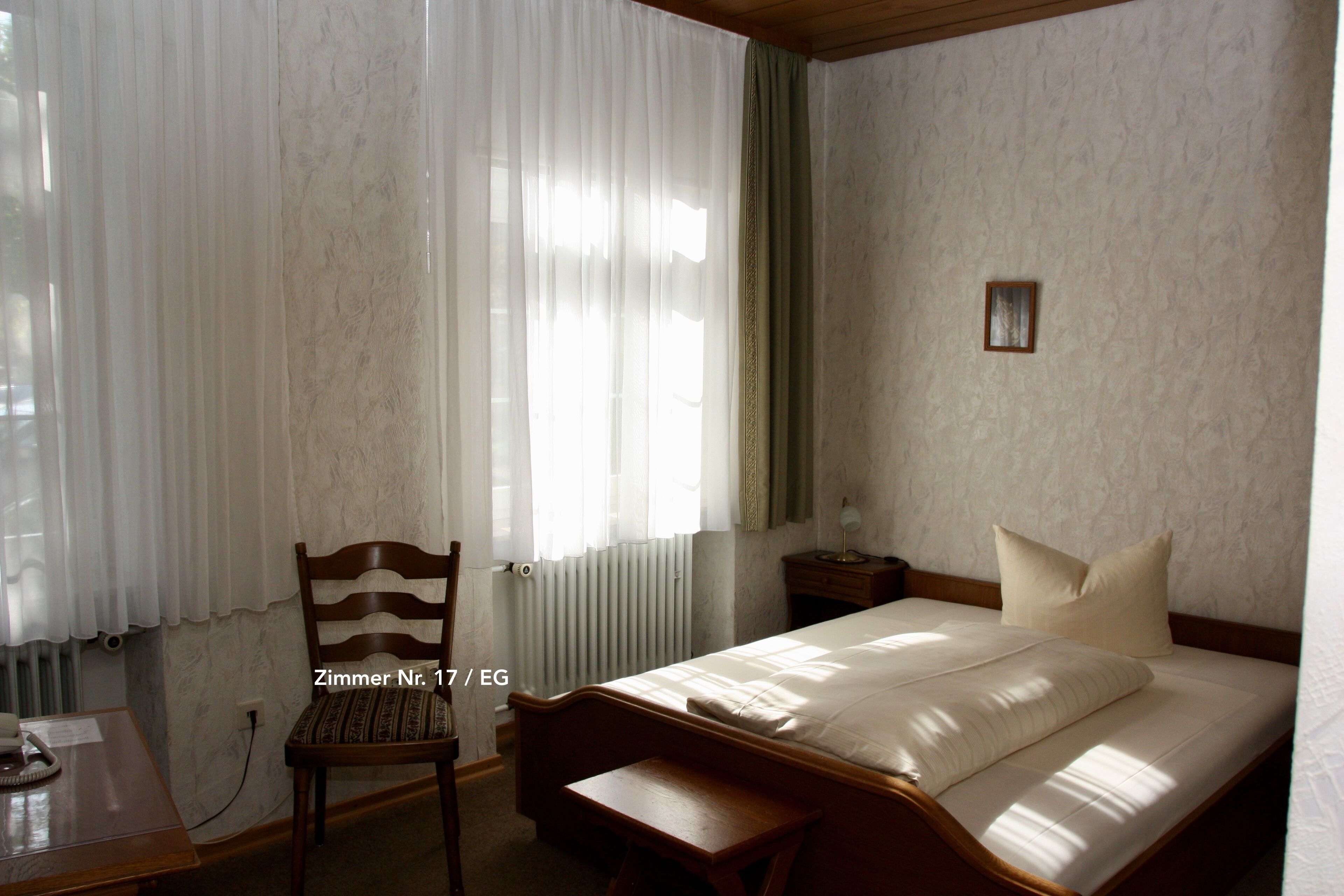 A bedroom with a bed, a chair, a bedside table, and a window with curtains.