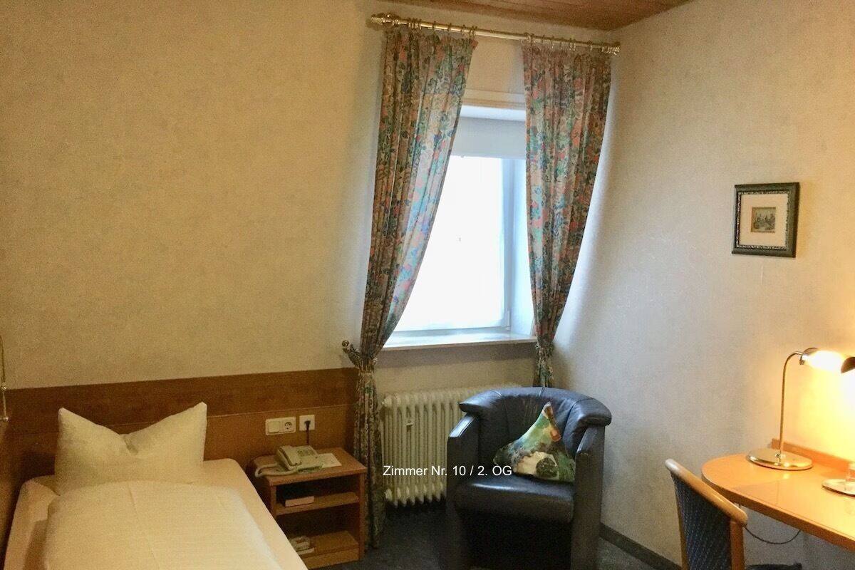 A hotel room with a bed, a chair, a desk, and a window with curtains.
