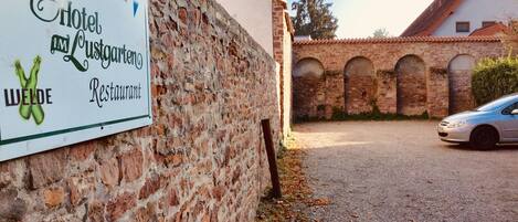 A sign for Hotel Zum Lusten Gasthof with a brick wall and a building with arched windows in the background.