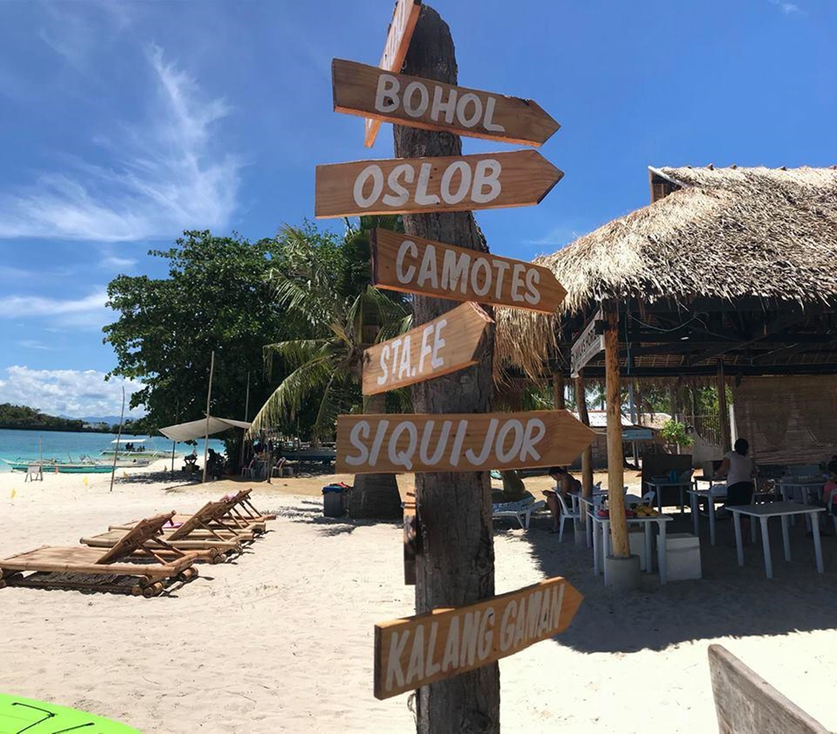 Een houten bord met verschillende richtpijlen die wijzen naar diverse locaties, zoals BOHOL, OSLOB, CAMOTES, STA. FE, SIQUIJOR en KALANG CAMAN.