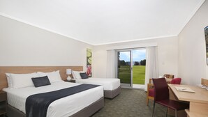 A hotel room with two beds, a desk, and a chair. There is a large window with a view of a green field. - Springs  Shoalhaven (Worrigee)
