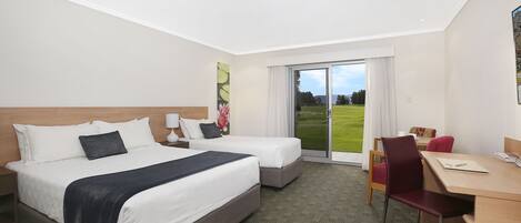 A hotel room with two beds, a desk, and a chair. There is a large window with a view of a green field.