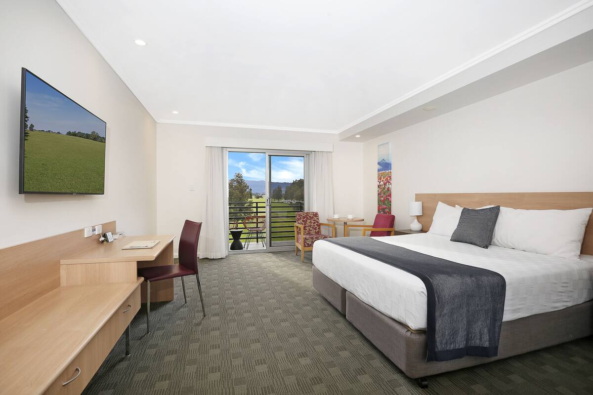 A hotel room with a bed, desk, chair, and a large window with a view.