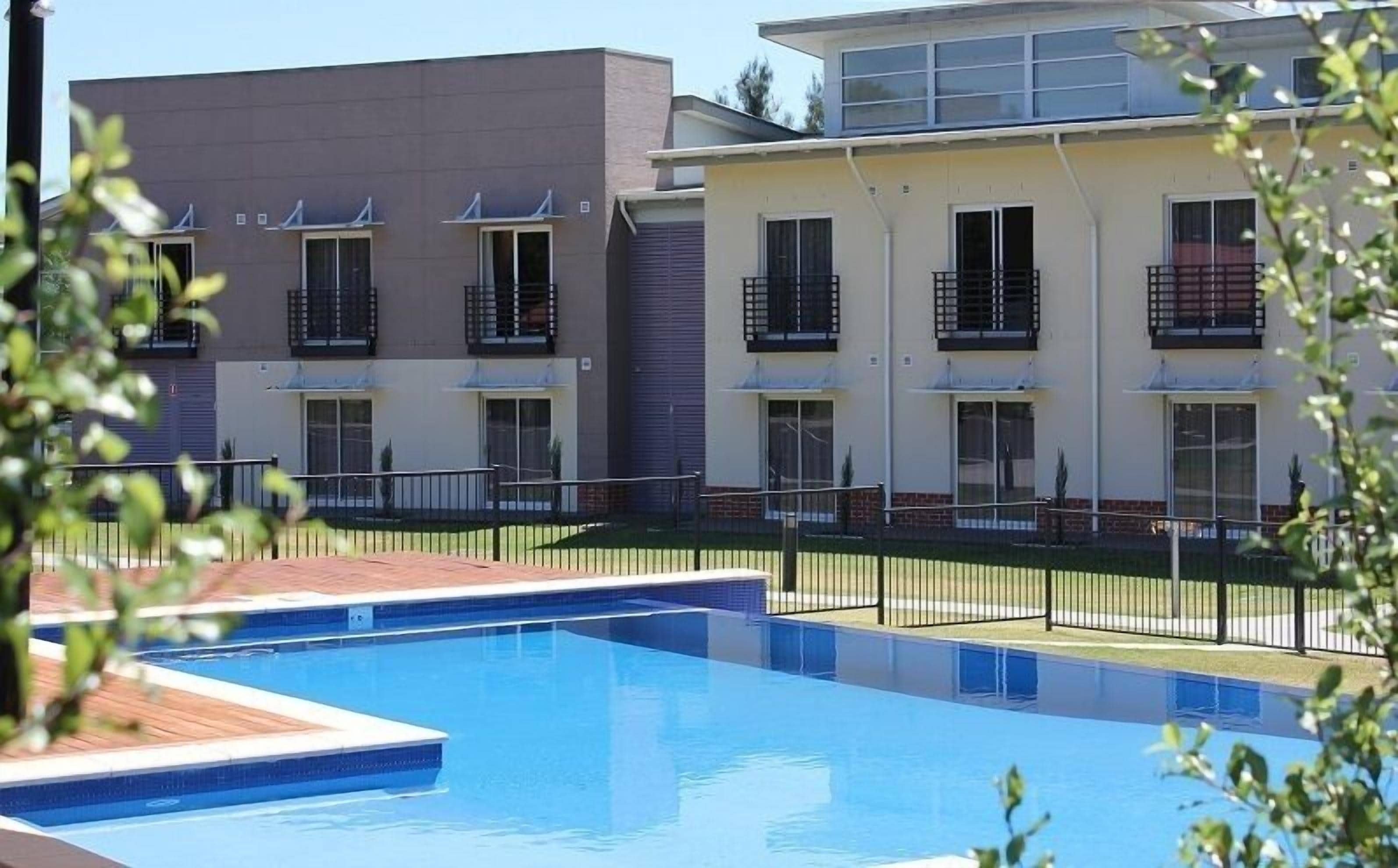 Una piscina con suelo de baldosas, rodeada por una valla de metal negro.