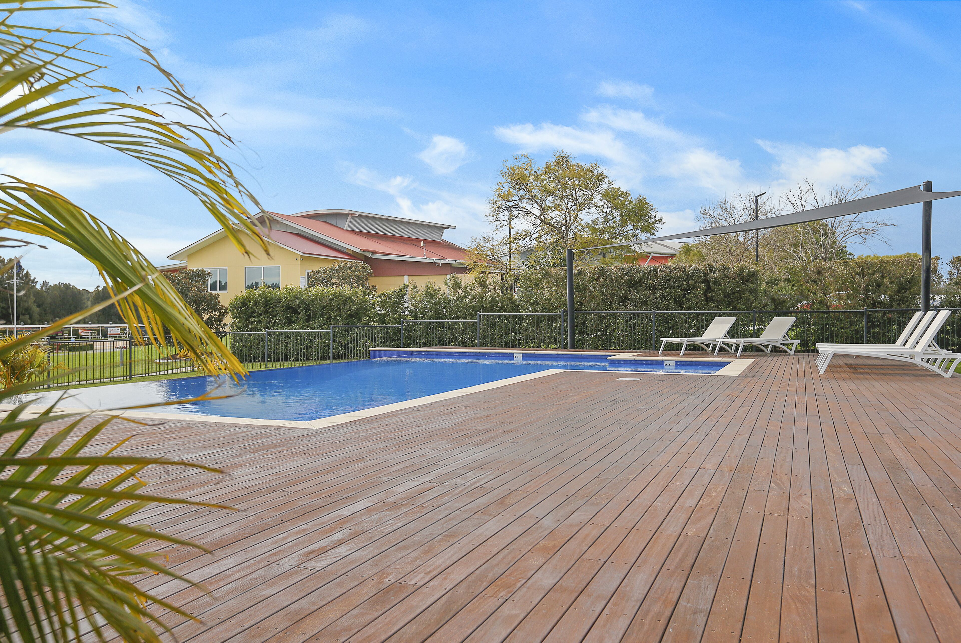 A wooden deck with a swimming pool, lounge chairs, and a house in the background.