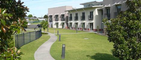 A modern building with a paved walkway, green lawn, and a fence.