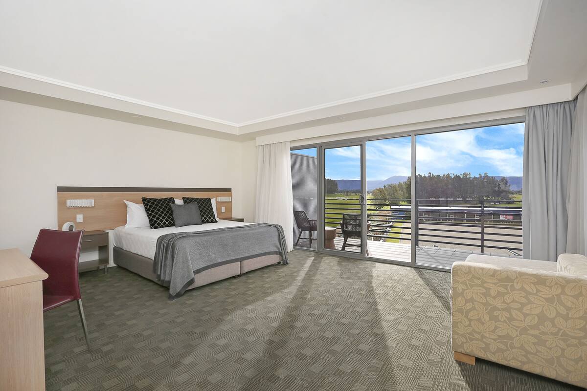 A hotel room with a bed, a desk, a chair, and a balcony with a view of the outdoors.