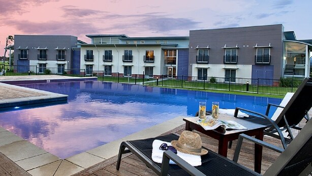 A modern hotel with a swimming pool, lounge chairs, and a view of the building's exterior. - Springs  Shoalhaven (Worrigee)