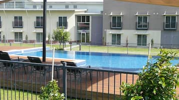 A swimming pool with lounge chairs, surrounded by a fence, and adjacent to a multi-story building with balconies.