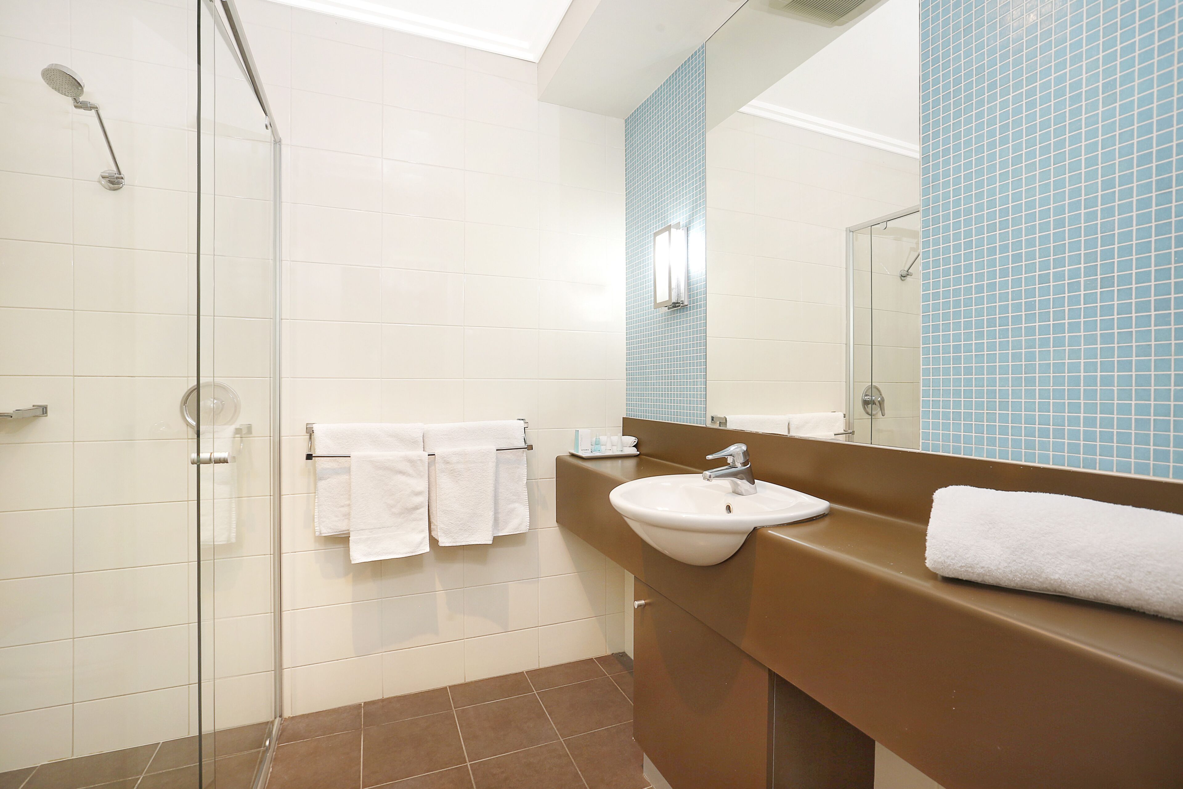 A bathroom with a glass shower enclosure, a sink, and a mirror.