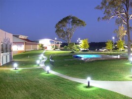 A well-lit outdoor area with a swimming pool, a building with a red roof, and a large tree.
