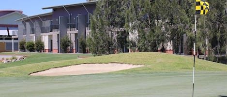 A golf course with a sand bunker, a flagstick, and a building in the background.
