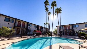 A swimming pool with lounge chairs, palm trees, and a building with multiple balconies.
