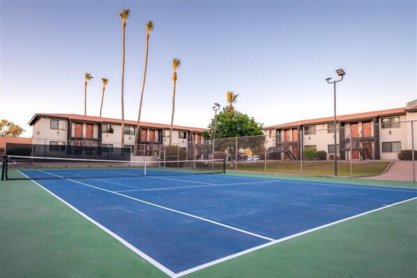 A tennis court with a net, surrounded by buildings with balconies and palm trees. - 210 Scottsdale Escape: Fully Furnished Vacation Rental with Resort Amenities (Scottsdale)