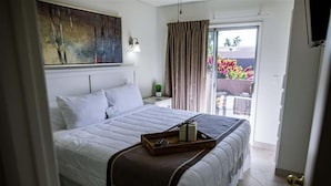 Een slaapkamer met een bed, nachtkastje, schilderij, gordijn en uitzicht.