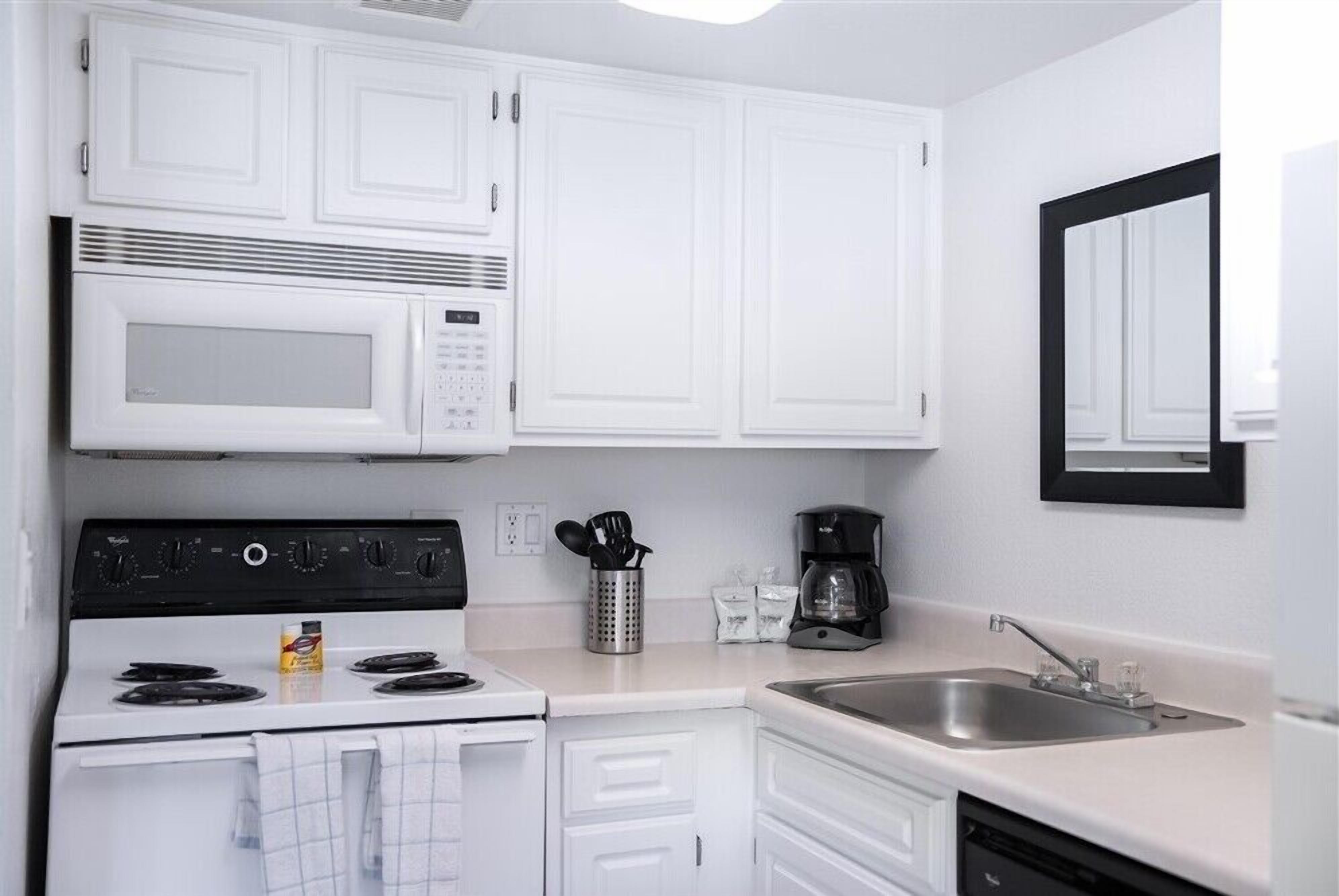 A modern kitchen with white cabinets, a microwave, stove, sink, and a coffee maker.