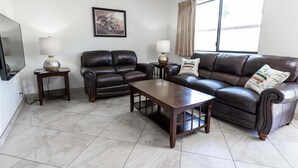 A living room with a leather sofa, a wooden coffee table, two side tables with lamps, a flat-screen TV, and a framed picture on the wall. - 143 Fully Furnished 1BR Suite-Pet Friendly! (Scottsdale)