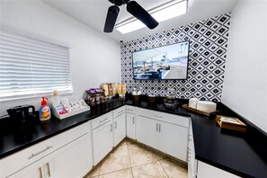 Una cocina moderna con encimera negra, armarios blancos, ventilador de techo y un televisor grande montado en una pared con diseño.