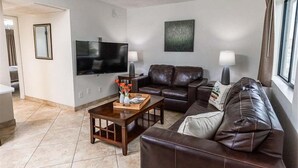 A living room with a flat-screen TV, leather couches, a coffee table, and a window with curtains. - 122 Luxury Greenbelt Escape | Private Patios, Spa, Pool & Outdoor Lounge for Relaxing Stays (Scottsdale)