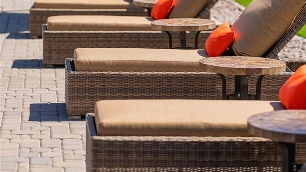 Outdoor wicker lounge chairs with cushions, a large umbrella, and a paved walkway. - 122 Luxury Greenbelt Escape | Private Patios, Spa, Pool & Outdoor Lounge for Relaxing Stays (Scottsdale)