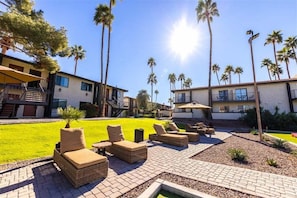 A courtyard with outdoor seating, palm trees, and a building with a staircase.