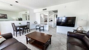 A modern living room with a sofa, a coffee table, a TV, and a dining area with chairs and a table. - 142 Fully Furnished 1BR Suite-Pet Friendly! (Scottsdale)
