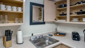 A kitchen with a sink, countertop, and shelves with cups and glasses. - 142 Fully Furnished 1BR Suite-Pet Friendly! (Scottsdale)