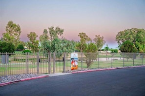 A fenced area with a sign, trees, and a road.