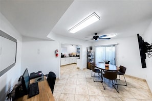 A modern kitchen with white cabinets, a dining area with a round table and chairs, a ceiling fan, and a visible fire extinguisher.