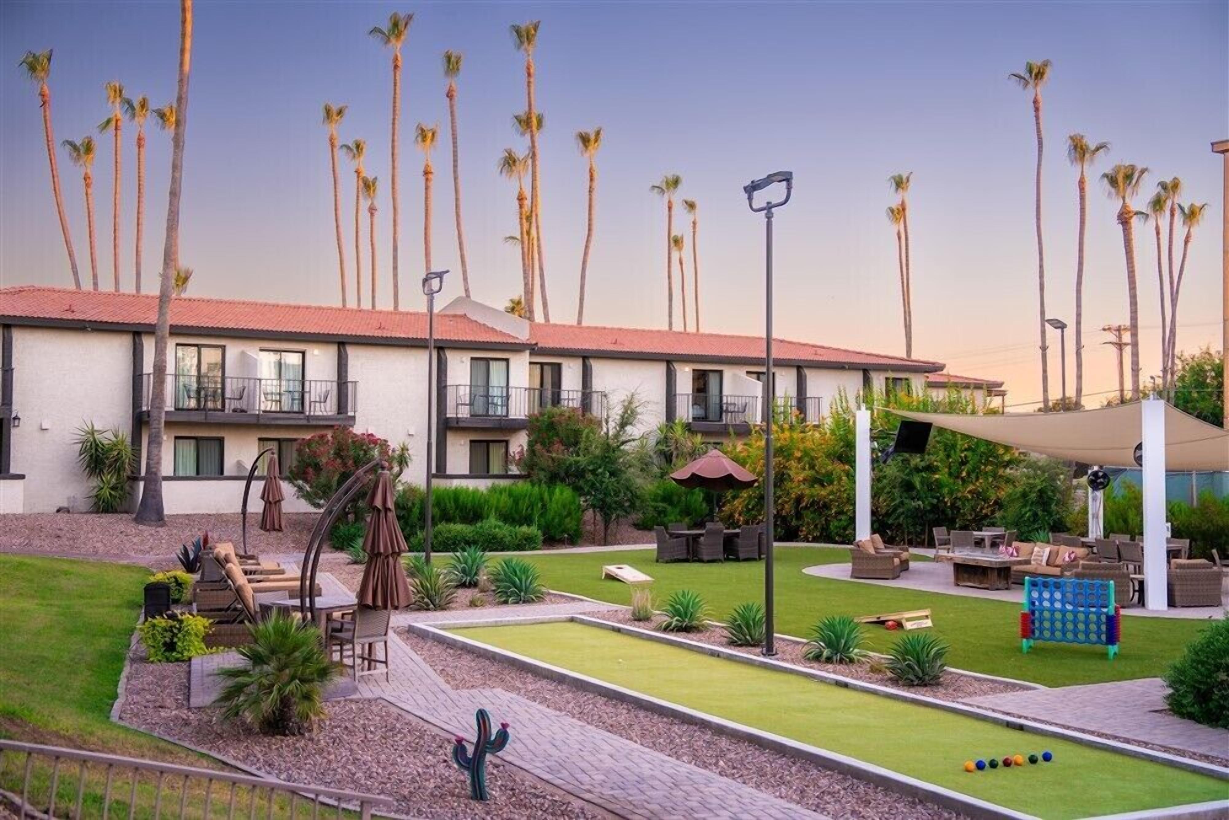Un hôtel doté d’un patio avec des espaces de détente en plein air, un terrain d’entraînement au golf et des palmiers.