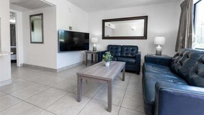Una sala de estar moderna con un televisor de pantalla plana, sofás de cuero, una mesa de centro y un espejo grande.