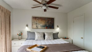 A bedroom with a bed, a ceiling fan, a painting, bedside lamps, a nightstand, and a tray with remote controls. - 147 Fully Furnished 1BR Suite-Pet Friendly! (Scottsdale)