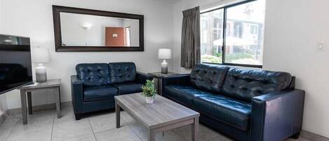 A modern living room with a dark leather sofa, a wooden coffee table, a flat-screen TV, and a large window with curtains.