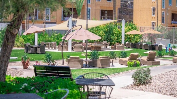 Un patio al aire libre con mobiliario de mimbre, sombrillas y un césped cuidado.
