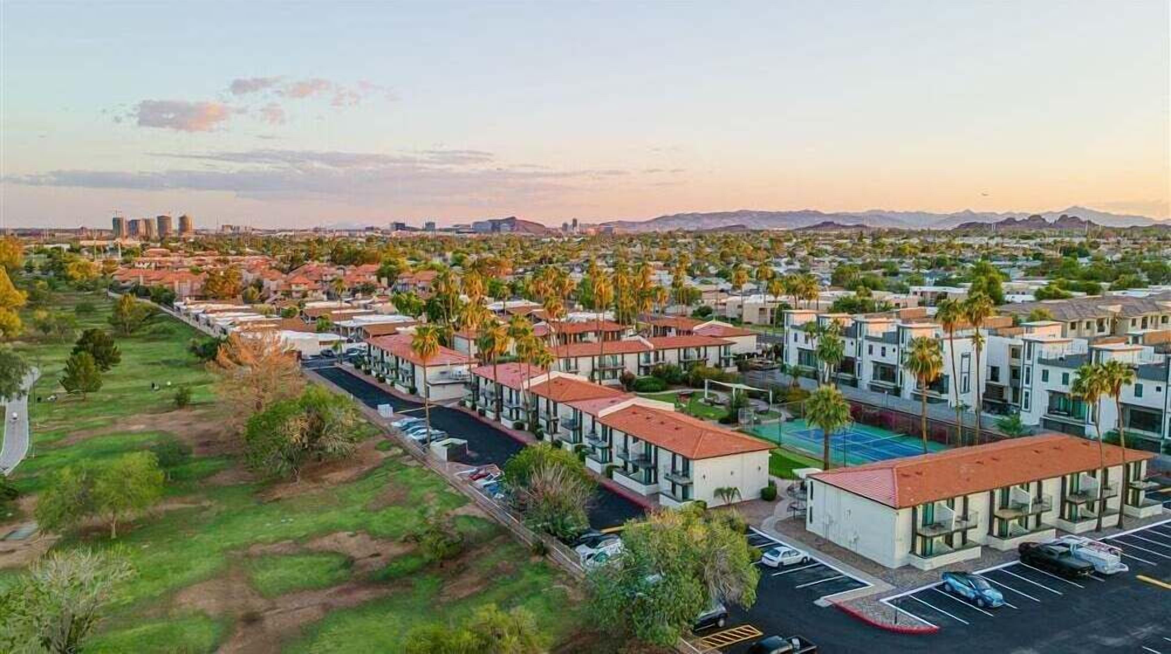 Un quartier résidentiel avec des maisons modernes, un court de tennis et une vue lointaine sur les gratte-ciel de la ville.