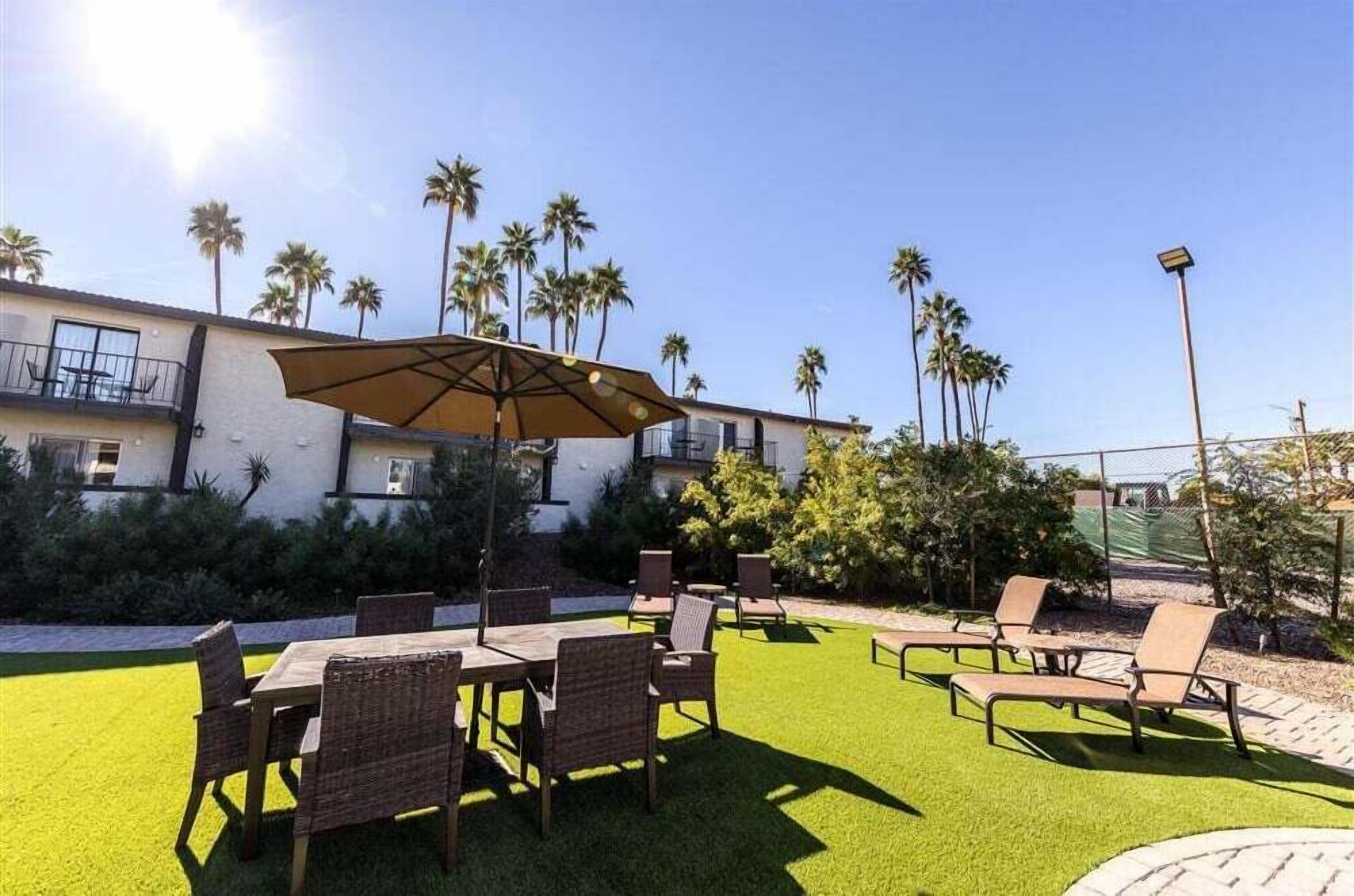 An outdoor patio with a table and chairs, surrounded by palm trees and a building.