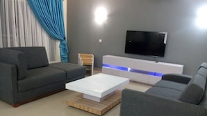 A modern living room with grey sofas, a white coffee table, and a TV mounted on the wall. - Amara Suites Banana Island (Lagos)
