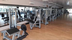 A gym with various exercise machines, large windows, and a wooden floor. - Amara Suites Banana Island (Lagos)