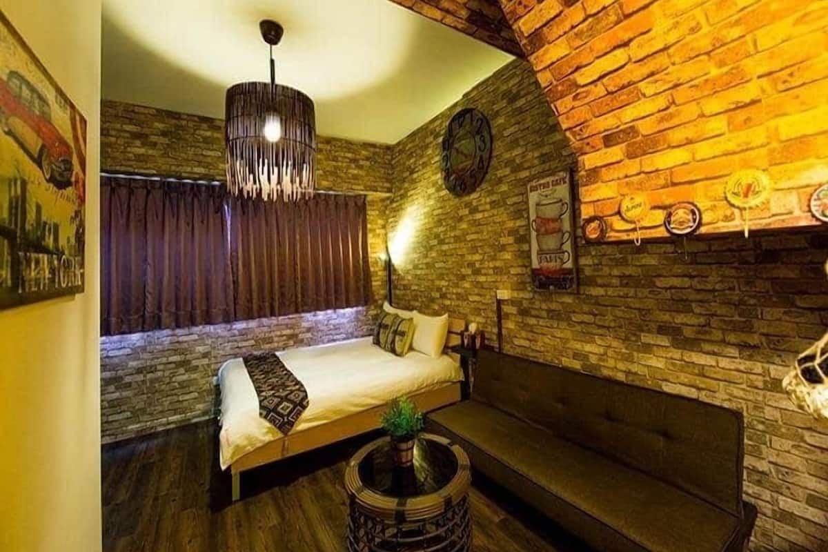 A cozy room with a bed, a sofa, a hanging light fixture, and a brick wall.