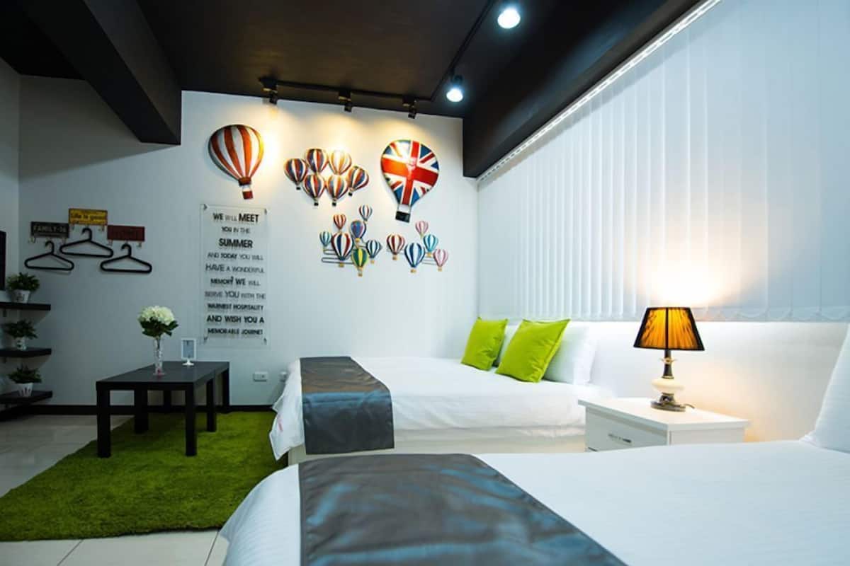 A hotel room with two beds, a green rug, a small table with a vase, and a wall with a message and hot air balloon decorations.