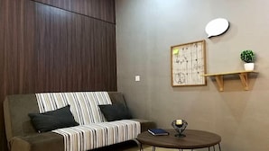 Una sala de estar moderna con un sofá, una mesa redonda, un estante en la pared con una planta y una obra de arte enmarcada.
