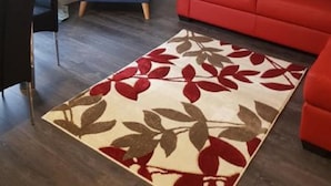A living room with a blue armchair, a red sofa, a patterned rug, and a painting on the wall.