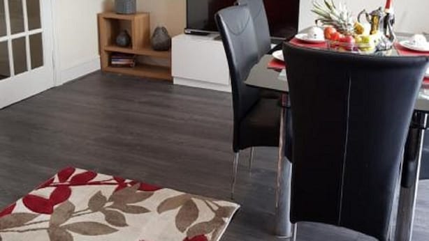 A modern living room with a dining area, a flat-screen TV, a red pendant light, and a floral rug.