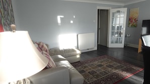 A living room with a sofa, a patterned rug, a lamp, a radiator, and a door leading to another room.