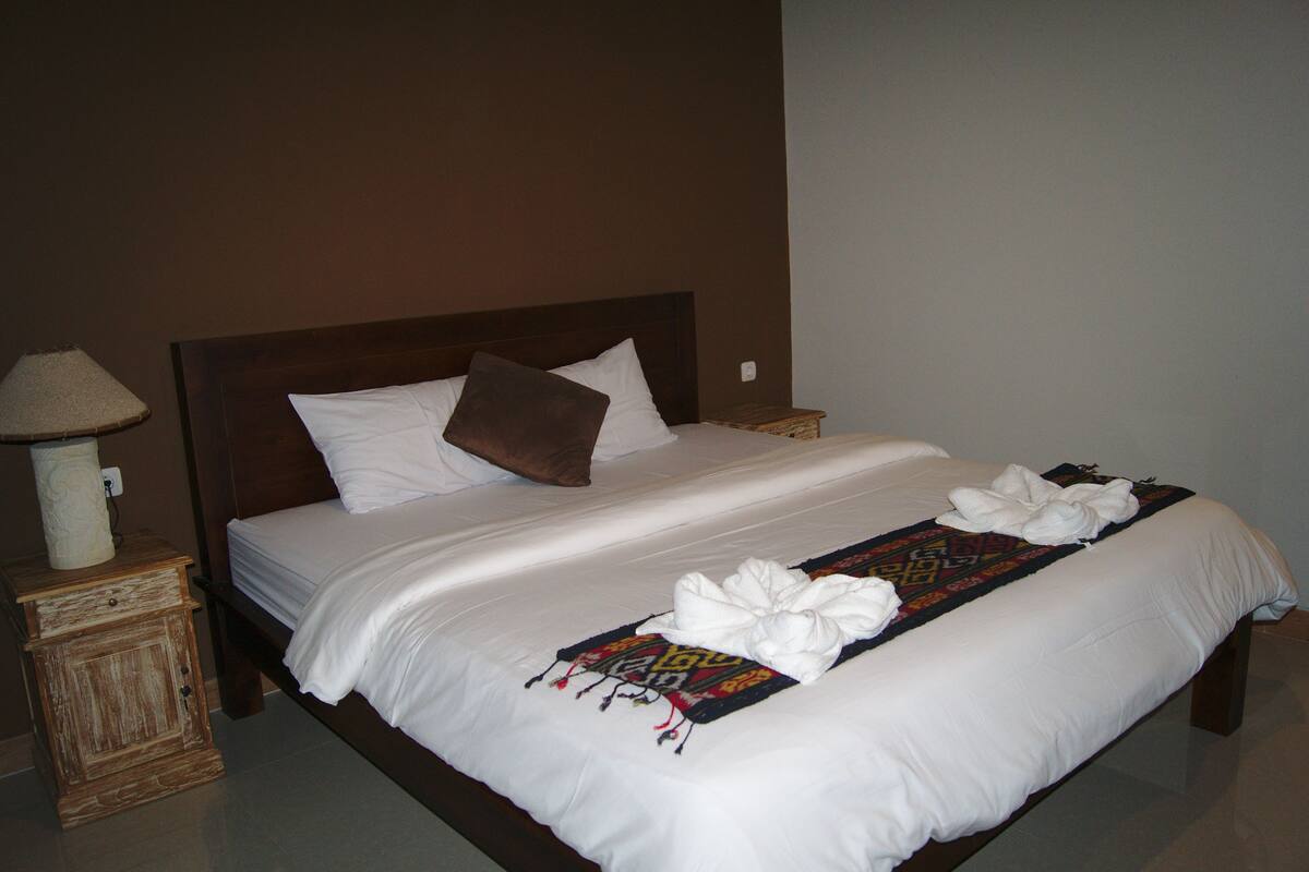 A neatly made bed with white linens, a brown pillow, and a decorative towel on the bed.