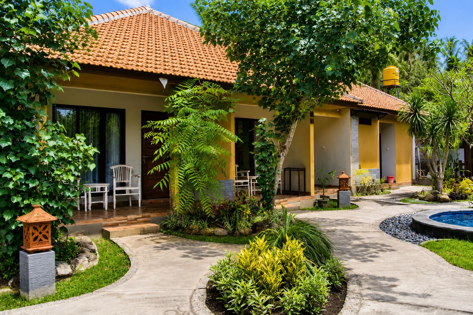 A two-story building with a tiled roof, a pool, and a garden with various plants and a small fountain.